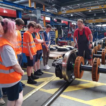 Gruppe besichtigt die Achse mit Rädern eines Zugs in der Wekstatt