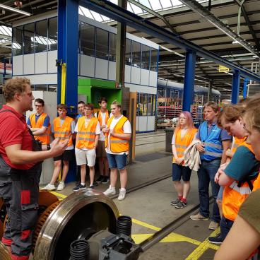 Gruppe besichtigt die Achse mit Rädern eines Zugs in der Wekstatt